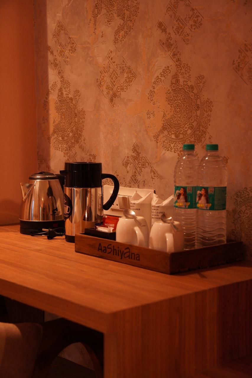 Une table en bois avec une machine à café, une bouilloire, une théière et deux bouteilles d’eau.