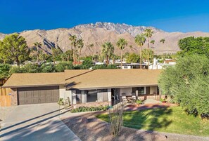 A modern house with a garage, a covered patio, and a mountain backdrop.