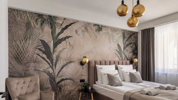 Une chambre à coucher moderne avec un grand lit, un fauteuil à capitons, une petite table d’appoint et une fresque murale.