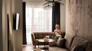 Un salon moderne avec un canapé, une petite table ronde et une grande fenêtre ornée de rideaux légers.