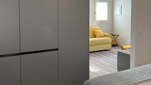 Une chambre à coucher moderne avec une armoire grise, un lit recouvert d’une couverture à motifs et un canapé jaune en arrière-plan.