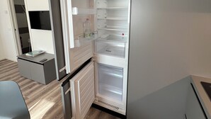 Une cuisine compacte dotée d’un réfrigérateur encastré, d’un petit plan de travail et d’une chaise.
