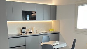 Une cuisine moderne avec des meubles gris, un four encastré et un coin repas comprenant une table ronde et deux chaises.