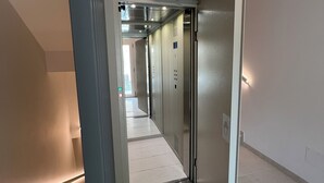 Un ascenseur moderne avec une finition métallique, un symbole représentant une main indiquant une zone d’atterrissage sécurisée, et un sol carrelé et impeccable.
