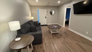 A modern living room with a gray sofa, two wooden side tables, a round coffee table, a mirror, and a TV mounted on the wall. - Central to Zoo and Baxter Arena, Pet Friendly (Omaha)