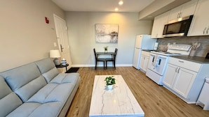 A modern living room with a sofa, a coffee table with a plant, and a dining area with chairs. - Close to Aksarben Village, Walk to Baxter Arena (Omaha)