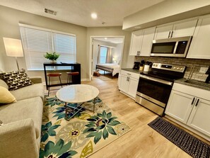 A compact living space with a kitchenette, a dining area with a round table, and a bedroom visible through an open door. - Aksarben Bliss, Quick I-80 Access, Free Parking (Omaha)