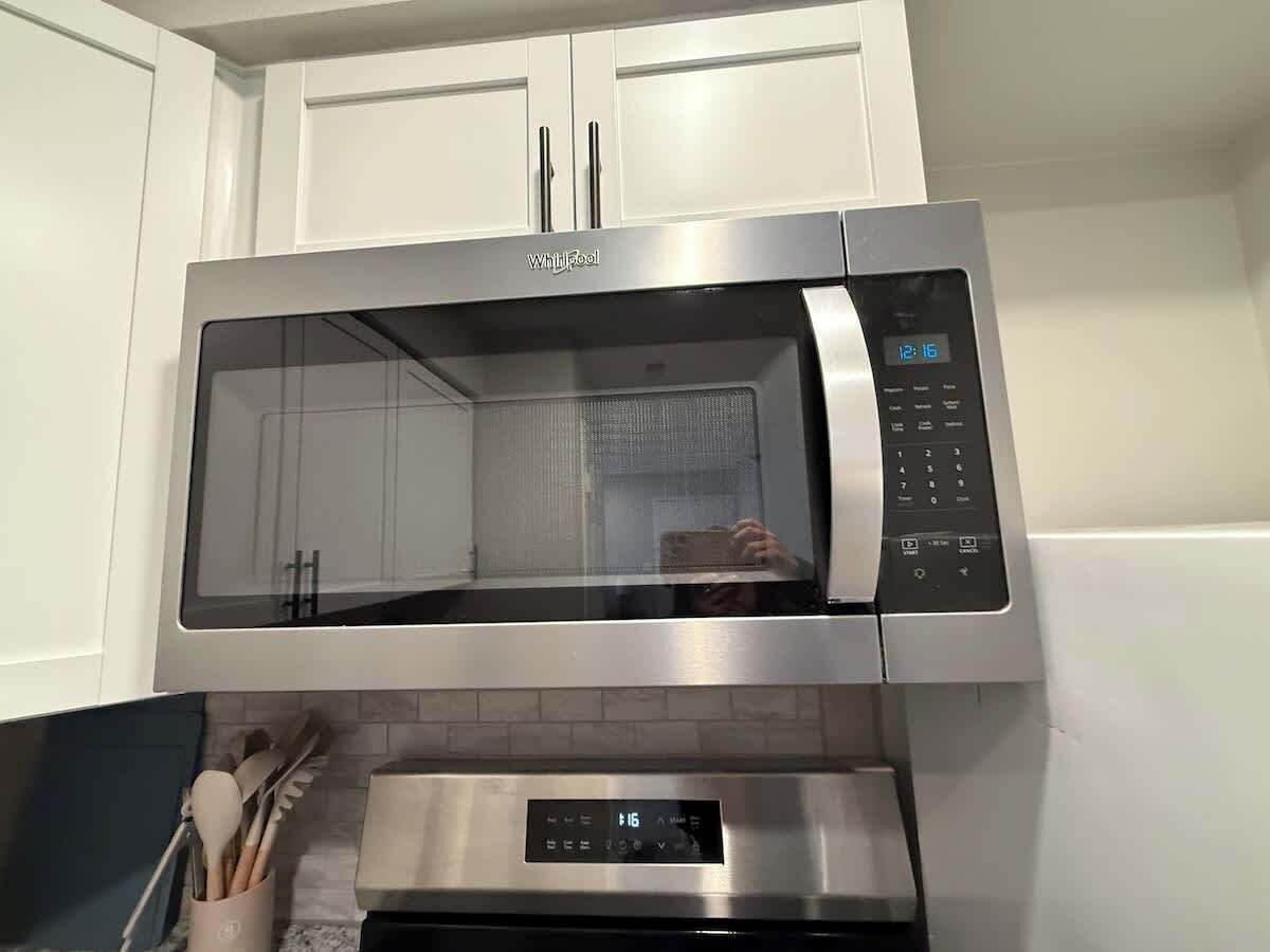 A stainless steel microwave oven with a digital display and control panel, mounted above a stainless steel oven.