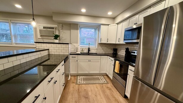 Una cocina moderna con armarios blancos, un refrigerador de acero inoxidable y una encimera negra.