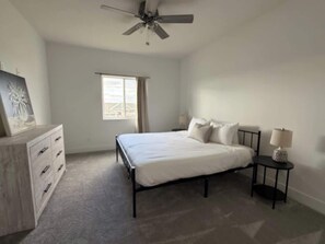 A bedroom with a bed, a dresser, a nightstand, a ceiling fan, and a window. - Spacious Family Retreat with Deck & Garage Access (Papillion)