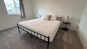 Een slaapkamer met een bed, twee nachtkastjes, een raam met gordijnen en een uitzicht op een huis.