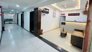A reception area with a reception desk, a sofa, a fire extinguisher, and a ceiling fan. - Hotel Pleasure (Surat)