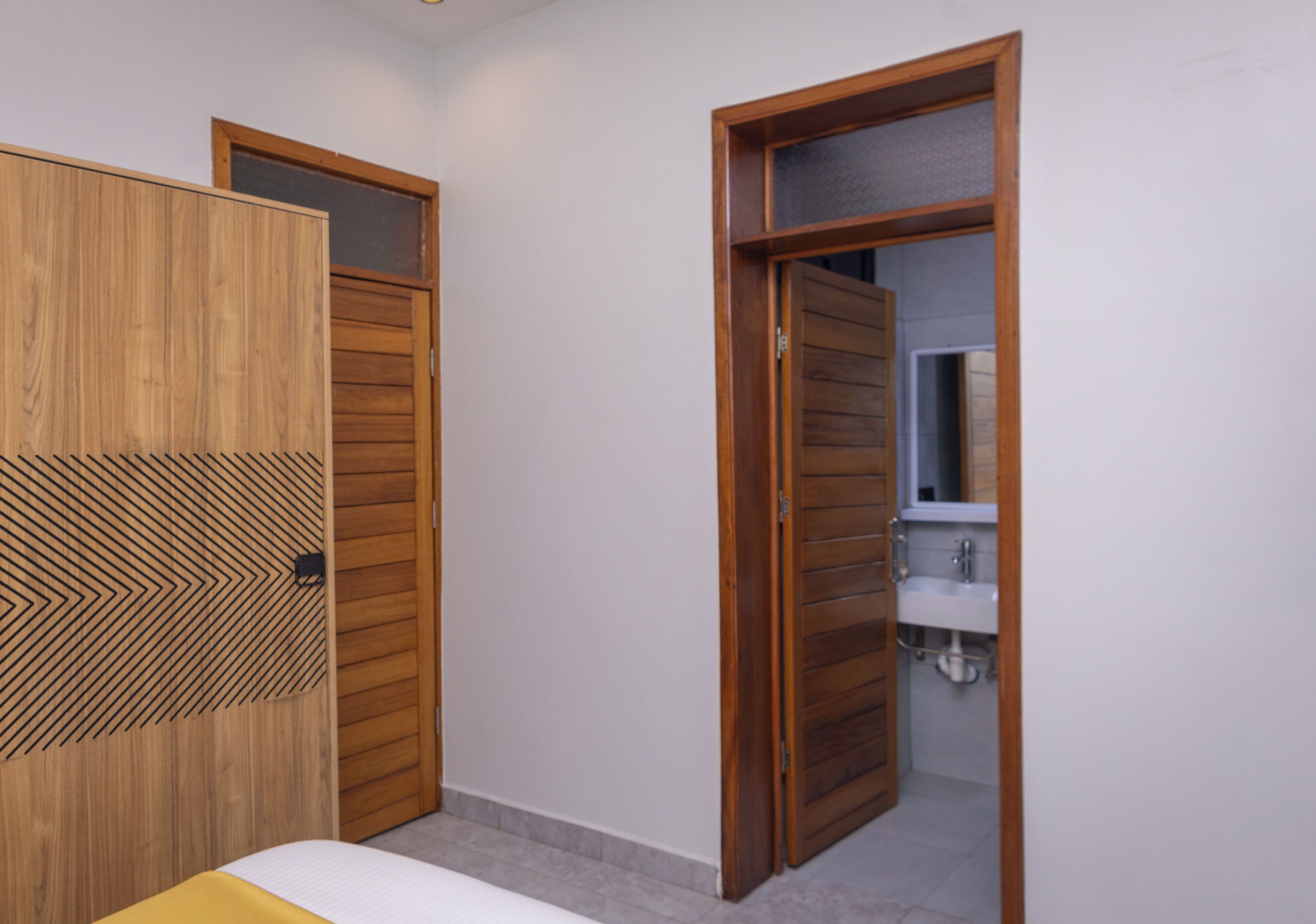 Ein Schlafzimmer mit Holzschrank, Bett und angrenzendem Badezimmer, das durch eine offene Tür sichtbar ist.
