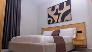 A modern bedroom with a large bed, a wooden headboard, a bedside table, and a wall-mounted abstract artwork. - Serene Apartment (Kigali)