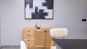 A modern room with a wooden cabinet, a white chair, and a black and white abstract painting on the wall. - Serene Apartment (Kigali)