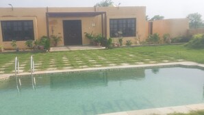 A modern building with a swimming pool, surrounded by well-maintained grass and potted plants. - Mura Yoga Villa (Kasrawad)