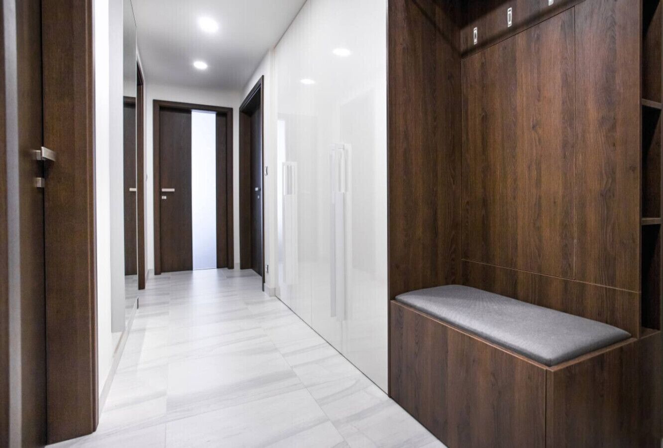 Un pasillo con un banco, paneles de madera y piso de baldosas blancas.