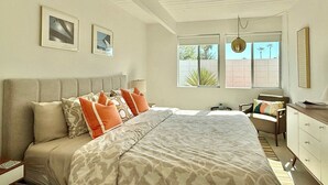 Un dormitorio con una cama grande, dos ventanas, un ventilador de techo y una mesita de noche.