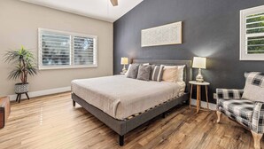 Une chambre à coucher avec un lit, un ventilateur de plafond, une fenêtre, une plante et une œuvre d’art accrochée au mur.