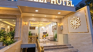 Das Hotel Nelly mit einem prunkvollen Eingang, einer gut beleuchteten Lobby und einem großen Blumenemblem an der Wand.