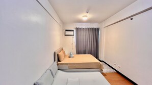 Ein kleines Zimmer mit einem Einzelbett, einem kleinen Tisch und einer Wand-Klimaanlage.