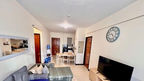 Ein Wohnzimmer mit Sofa, Hocker, Fernseher und Teppich.