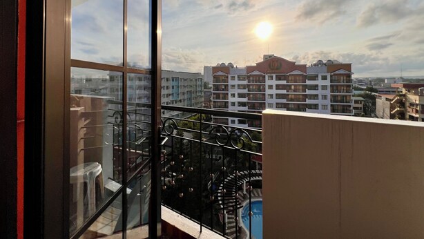 Ein Balkon mit Glastür, ein Pool und Blick auf eine Stadtlandschaft mit Gebäuden und einem untergehenden Sonnenuntergang.