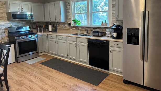A modern kitchen with stainless steel appliances, light gray cabinets, and a large window providing natural light. - Peaceful Plum PA Home (Pittsburgh)