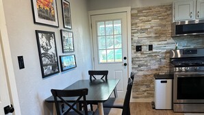 A modern kitchen with a dining area, featuring a stone backsplash, stainless steel appliances, and framed artwork on the wall. - Peaceful Plum PA Home (Pittsburgh)