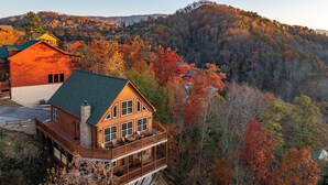 A wooden cabin with a balcony, surrounded by autumn foliage and hills. - Private Indoor Pool · Close 2 Dollywood · Mountain Views · Hot Tub + Game Room (Sevierville)