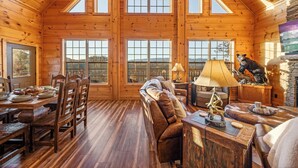 A spacious log cabin with a high ceiling, large windows, a fireplace, and a cozy seating area. - Private Indoor Pool · Close 2 Dollywood · Mountain Views · Hot Tub + Game Room (Sevierville)