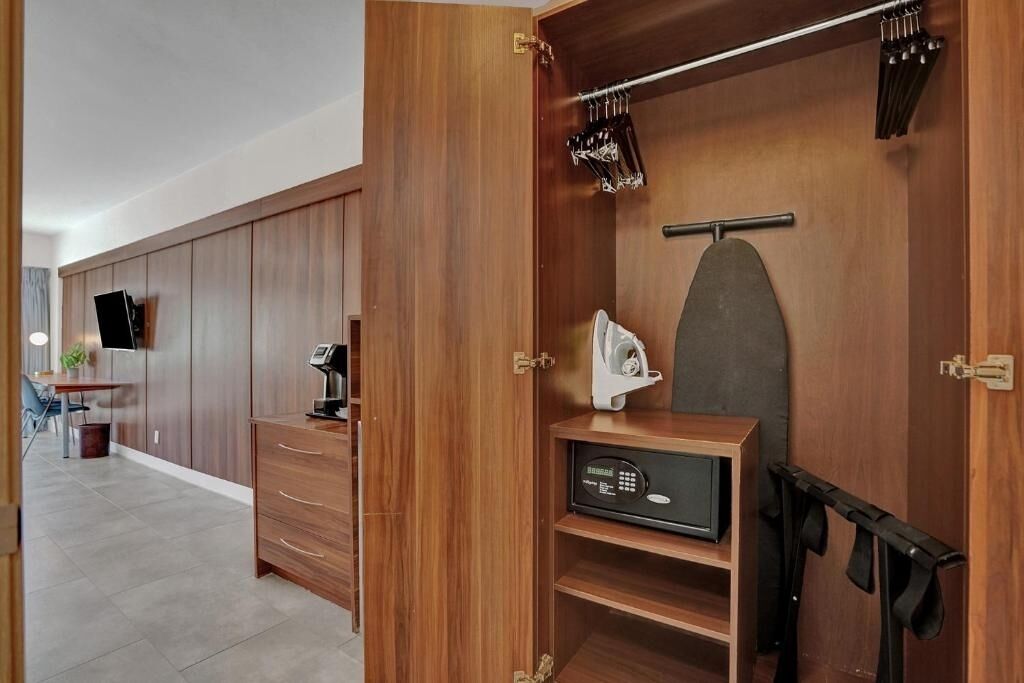 A modern room with a wooden wardrobe, a desk with a computer, and a small seating area.
