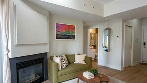 A living room with a fireplace, a sofa, a coffee table, and a painting on the wall. - 13th Ave Condo + City Views + Balcony + Walkable (Calgary)