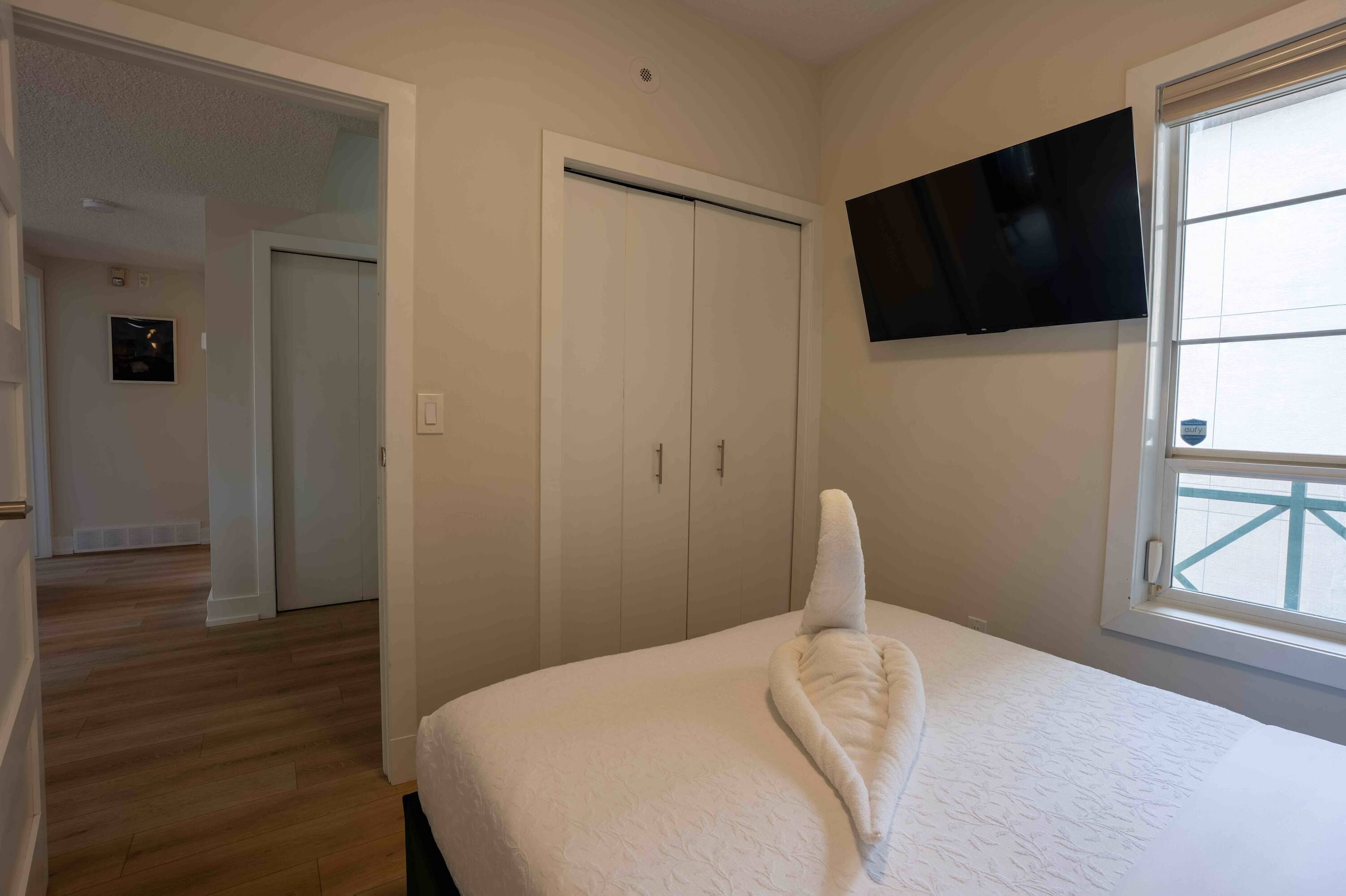 Quarto com cama, televisão na parede e janela.