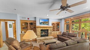 A cozy living room with a stone fireplace, leather sofas, and wooden shelves. - Ski-In/Ski-Out 3-Bedroom + Bunk Room Condo w/ Slope Views & Resort Amenities (Keystone)