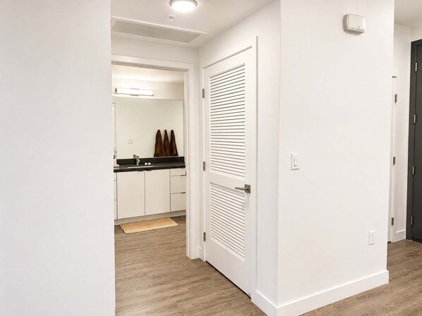 A hallway leading to a kitchen with white cabinets, a black countertop, and a door with horizontal slats.