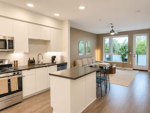 A modern kitchen with a central island, stainless steel appliances, and a dining area with a view. - Modern Apartment 10 Min to Disneyland | Pool & Gym (Santa Ana)