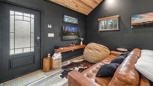 A modern living room with a leather couch, a wooden ceiling, and artwork on the walls. - Honeymoon Hideaway • Hot Tub • Fire Pit (Sevierville)
