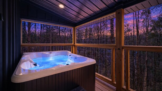 A hot tub in a wooden cabin with a view of a forest at dusk. - Honeymoon Hideaway • Hot Tub • Fire Pit (Sevierville)