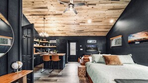 A modern bedroom with a large bed, a desk, and a kitchenette. - Honeymoon Hideaway • Hot Tub • Fire Pit (Sevierville)