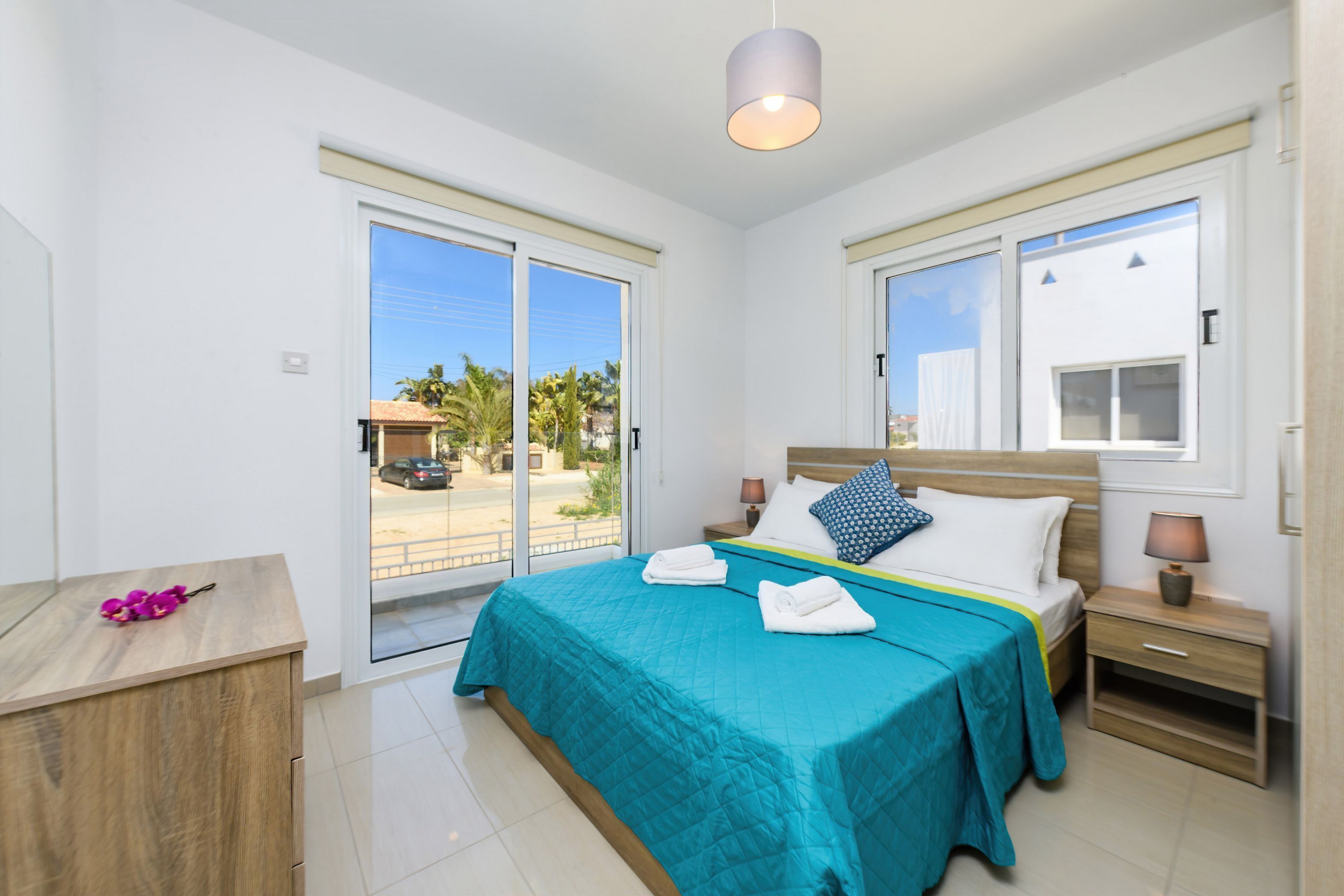 A bedroom with a large bed, a nightstand, a wooden desk, and a sliding glass door leading to an outdoor area.