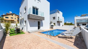 A modern pool area with a rectangular pool, lounge chairs, and a small table with chairs. - Nissini Villa 8 in Ayia Napa (Ayia Napa)