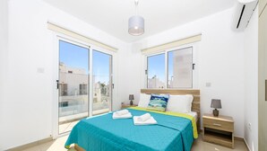 A bedroom with a large bed, a nightstand, a lamp, and a sliding glass door leading to an outdoor balcony. - Nissini Villa 8 in Ayia Napa (Ayia Napa)