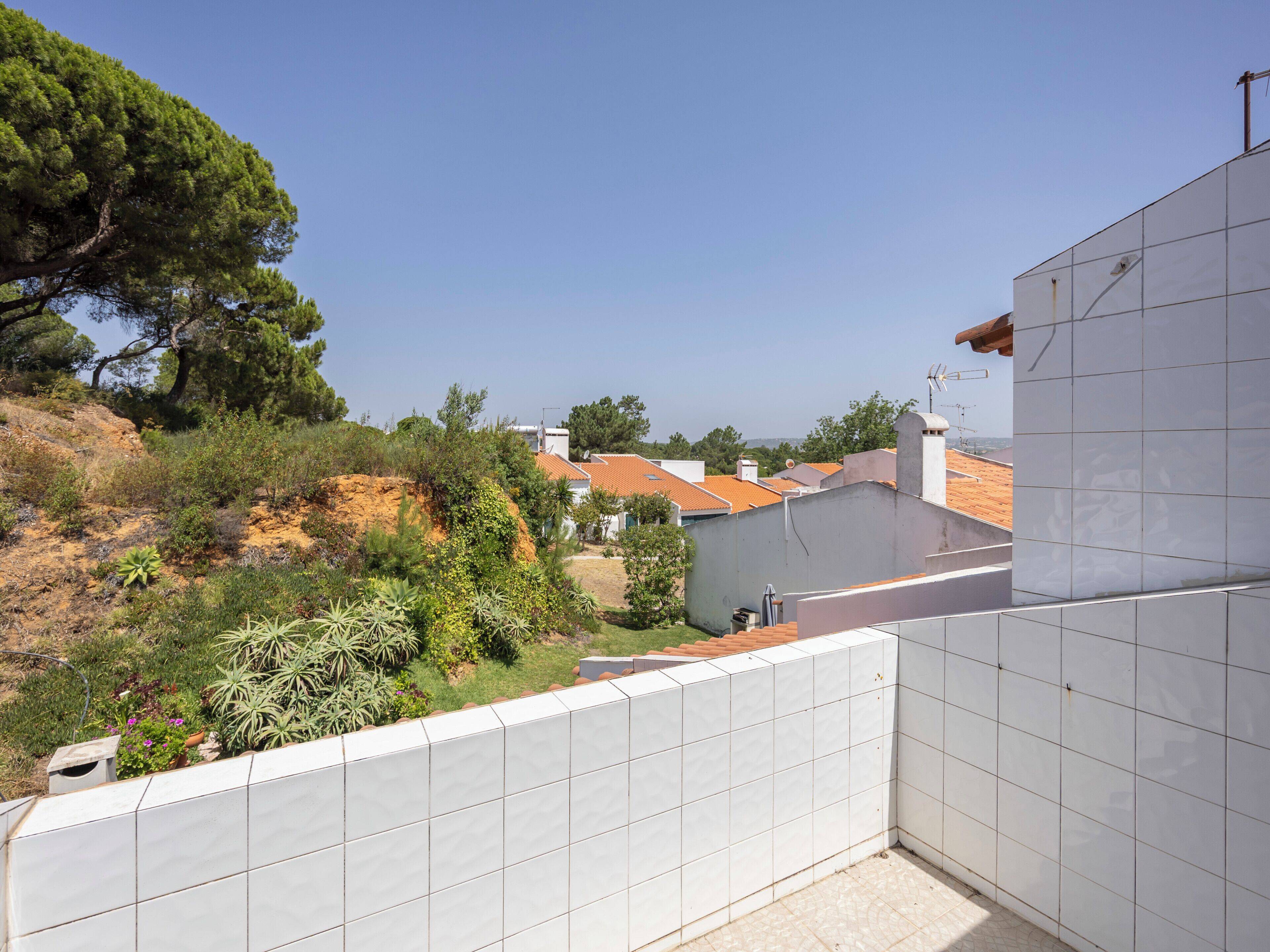 Un barrio residencial con un balcón con tejas, vistas a casas con tejados rojos y una ladera cubierta de vegetación.