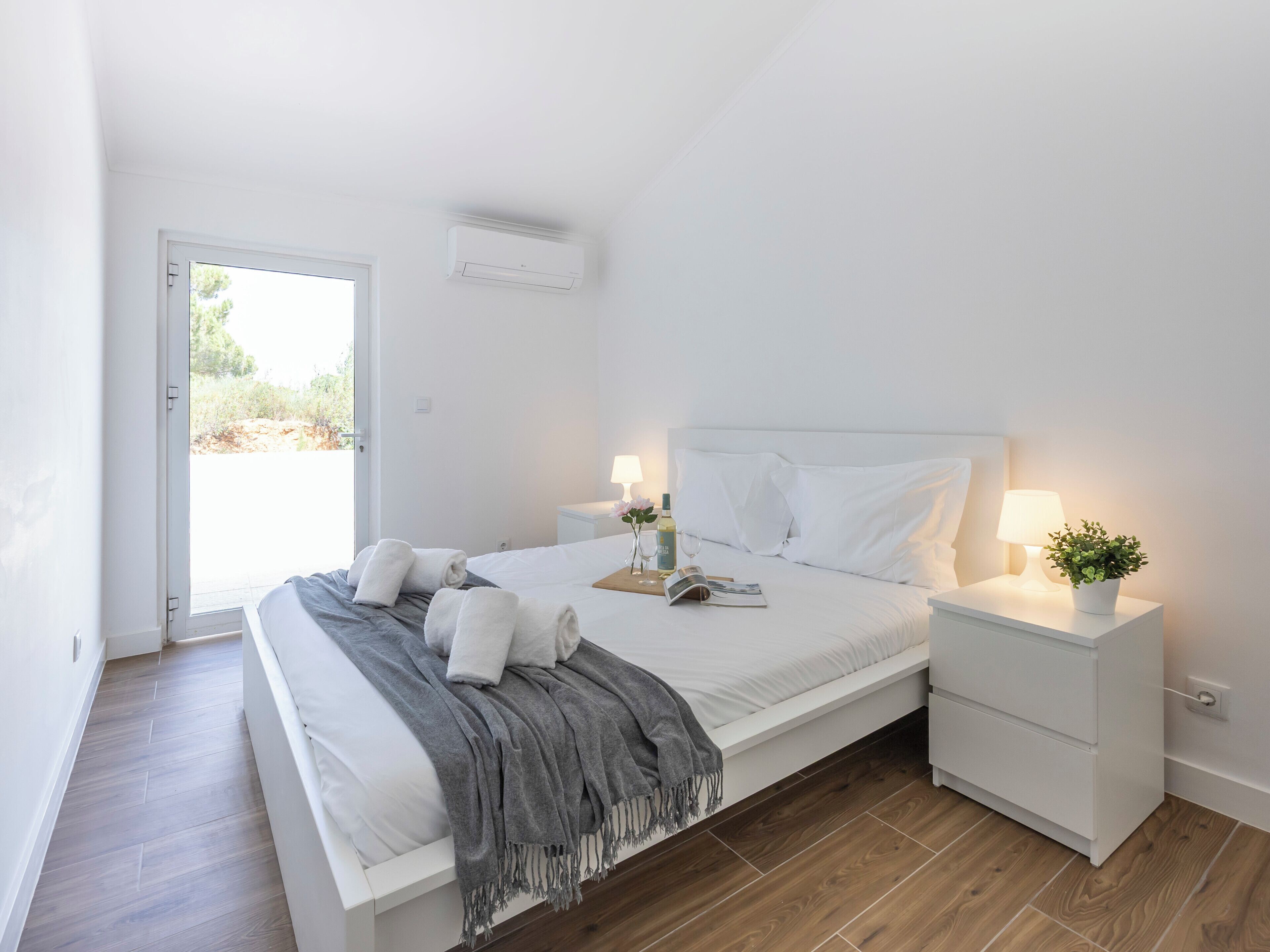 A modern bedroom with a bed, bedside tables, a small plant, and a window.