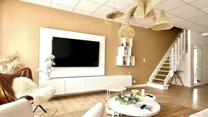Een moderne woonkamer met een grote flatscreen televisie, witte meubels, een trap en decoratieve rieten verlichting.