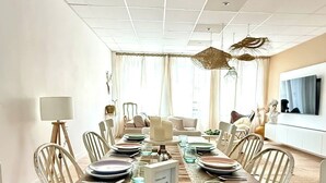 Een eetkamer met een lange houten tafel voor zes personen, omringd door witte stoelen.