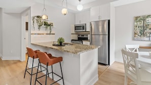 A modern kitchen with white cabinets, a granite countertop, stainless steel appliances, and a bar area with stools. - 13th Ave - DT Calgary - 2BD 2BA - Sleeps 5 (Calgary)