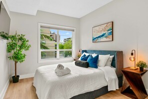 A bedroom with a bed, a window, a plant, and a painting. - 13th Ave - DT Calgary - 2BD 2BA - Sleeps 5 (Calgary)