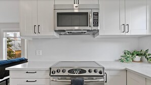 A modern kitchen with white cabinets, a stainless steel microwave, and an oven. - Local Loft Downtown Okotoks 2BD Private (Okotoks)